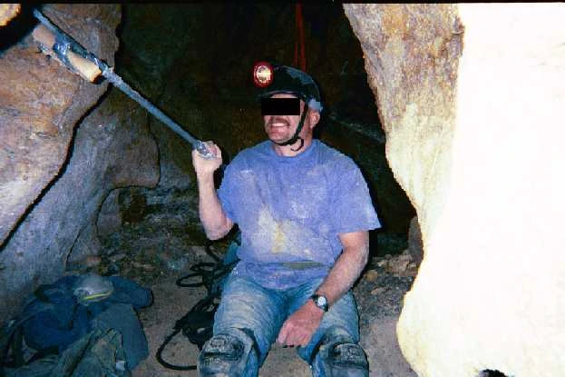 Here is a picture of B, edited to protect his identity, with the pipe we made. I took the picture, facing away from the Tomb. He is sitting on the rope bag that we used as a bed. Behind him to his left is the passage that leads down to the still water. Behind him to his right is the last drop-off before the passage. You can see some orange webbing we use to climb down and up
